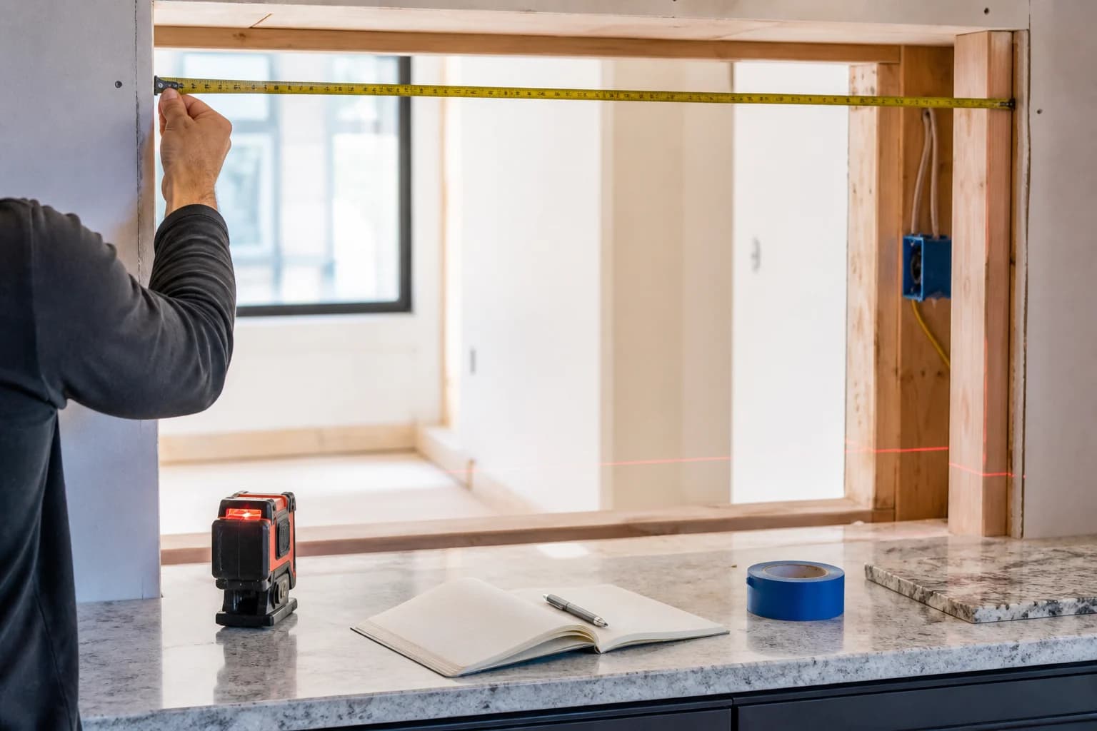 Professional measuring a rough opening above a kitchen counter
